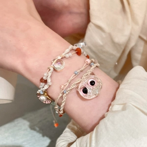 Detail of woven bracelet set with pink cat charm and sea shell pendant on wrist