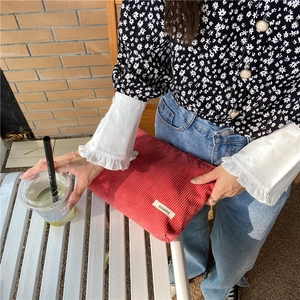 Detailed texture of red corduroy makeup bag held by hand in an outdoor setting