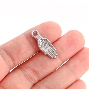 Close-up of a silver Hamsa Hand charm with evil eye detail held by hand in a high-detail view