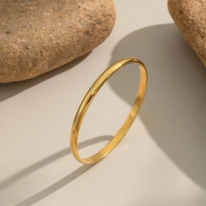 Detailed view of elegant gold minimalist stainless steel bangle set against natural stones