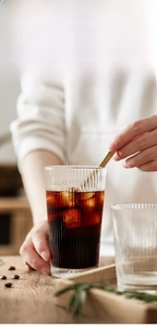 Close-up of hand stirring iced coffee in a ribbed glass with elegant lead-free texture