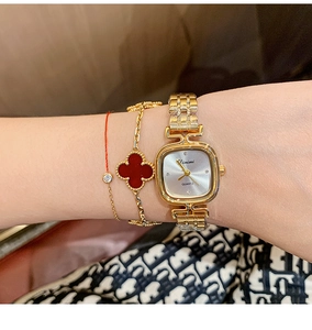 Close-up of a gold square quartz watch with a matching red clover bracelet on the wrist