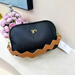 Detail of black pebbled leather camera bag with golden hardware and caramel wave strap