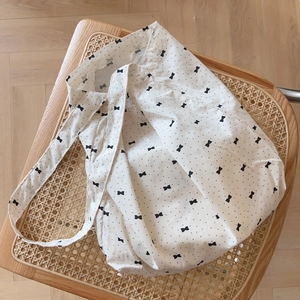 Sac fourre-tout en coton avec motifs nœuds noirs posé sur une chaise en rotin tissé