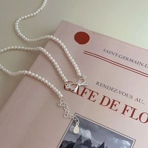 Detail of silver bow pendant and pearl necklace on a soft pink decorative book background