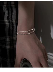 Detail of a layered silver-plated bracelet featuring a sparkling pavé chain and bead link
