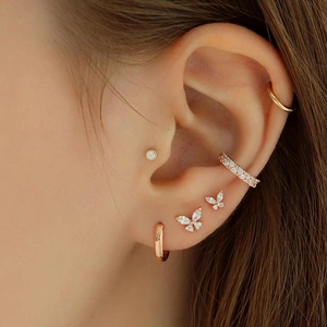 Close-up of gold butterfly screw back stud and crystal hoop earring set on ear