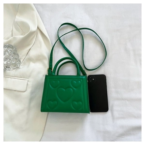 Détail d'un sac à main vert avec texture cœur 3D à côté d'un smartphone et d'un blazer