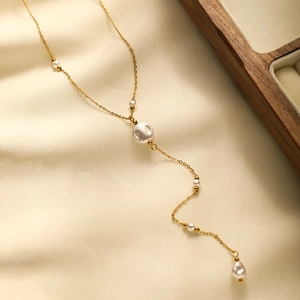 Detailed view of the gold-plated Y-shaped pearl tassel necklace on soft fabric background