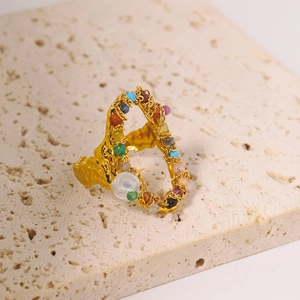 Detail of gold titanium ring with colorful beads and white pearl on beige stone