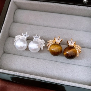 Close-up of gold tiger eye and silver pearl stud earrings in a luxury velvet jewelry box
