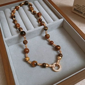 Detail of tiger eye beaded necklace with a gold diamond-set clasp on a gray velvet tray