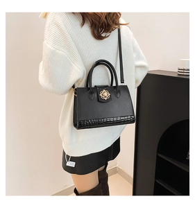 Detail of black crocodile embossed handbag featuring a gold floral metal clasp on the flap