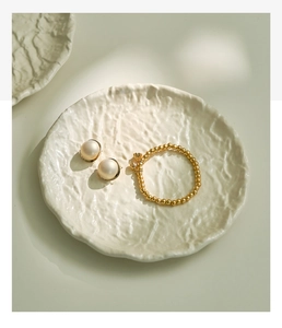 Detailed view of pearl earrings and gold bead bracelet on a wavy white ceramic tray
