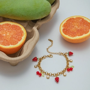 Detail of gold chain bracelet with strawberry and cherry charms on a fruit background