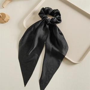 Elegant black silk scrunchie with long ribbon streamers on a minimalist tray