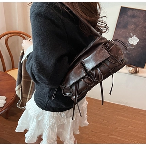 Detail of dark brown leather shoulder bag with pockets and ribbons on a model back