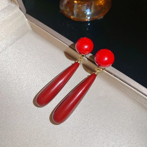 Detailed shot of red teardrop pearl earrings on beige velvet jewelry box with warm lighting
