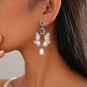 Detail of silver hollow butterfly earrings with green gemstone and white pearl on model