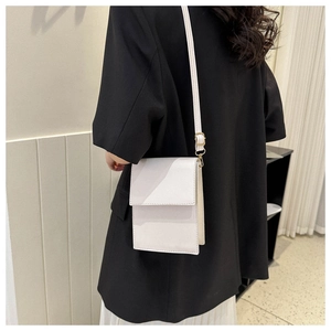 Détail d'un petit sac à bandoulière blanc rectangulaire porté sur un blazer noir