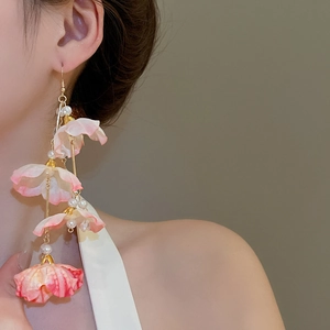 Détail de boucles d'oreilles fleurs en tissu rose avec de longs pompons et perles