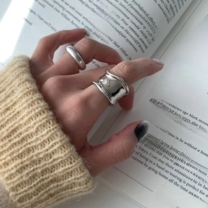 Detailed close-up of a wide wavy silver ring and slim band on a model wearing knitwear