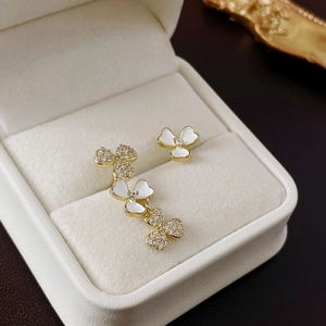 Detail of asymmetrical gold floral earrings with white enamel and clear zircon stones