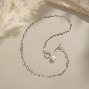 Detailed view of a silver paperclip chain necklace with a pearl pendant and OT buckle