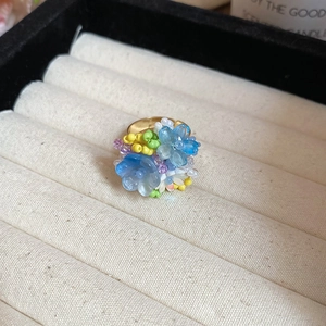 Dettaglio dell'anello con fiori di resina blu e perline con fascia dorata in astuccio
