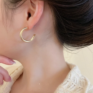 Close-up of a minimalist golden C-shaped hoop earring worn on a model's ear