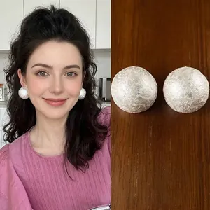 Minimalist silver pleated texture ball earrings shown on model and wooden background