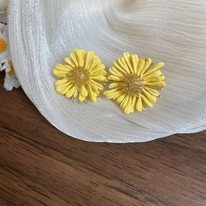 Gros plan détaillé de boucles d'oreilles marguerites jaunes en acrylique sur tissu texturé