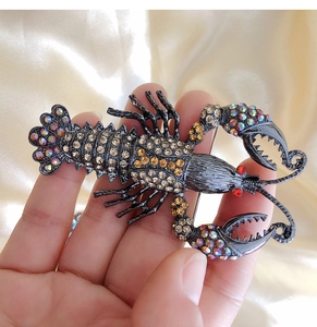 Detailed close-up of a lobster brooch featuring orange rhinestones on a dark metal base