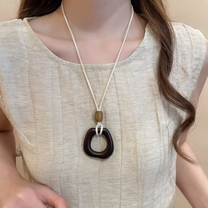 Detail of bohemian necklace featuring dark brown resin ring and amber bead on wax cord