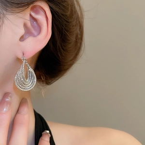 Close-up of a woman wearing silver multi-layered hollow twisted oval hoop earrings