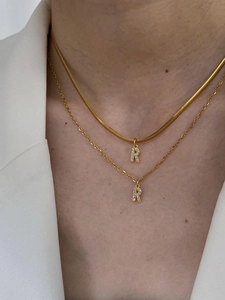 Close-up of golden layered necklaces with sparkling diamond-set R letter pendants