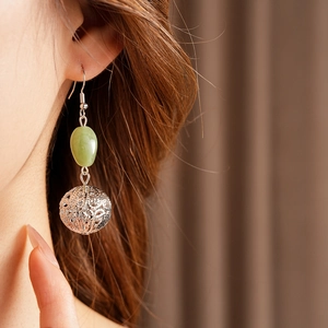 Close-up of a silver hollow metal ball and green oval bead drop earring on a model