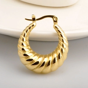 Elegant gold hollow twisted hoop earrings with a polished finish on white ceramic display