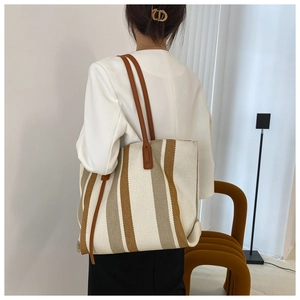 Detailed back view of a beige and yellow striped canvas tote bag worn by a model