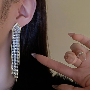 Detail of long gold tassel earrings with white rhinestones worn by a model in close-up