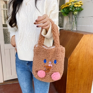 Detail of cute brown plush handbag with teddy bear embroidery held by a model in casual wear