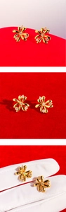 Close-up of golden flower stud earrings with white zircon accents on red background
