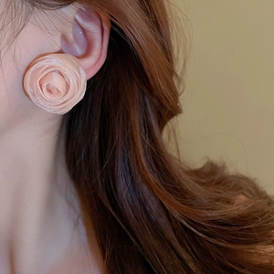 Close-up of pink fabric mesh flower earrings worn by a model with a soft beige background