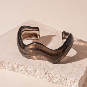 Macro detail of amber resin wavy open bangle featuring dark brown marble textures