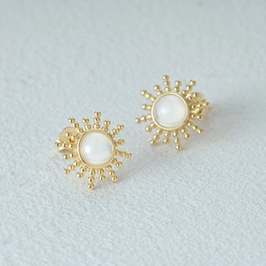 Macro shot of gold sunbeam stud earrings with white gemstone and vintage 925 silver texture