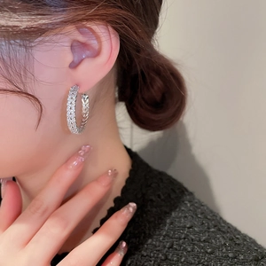 Close-up of a silver C-shaped hoop earring with shimmering zircons on a model's ear