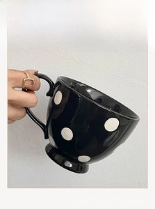 Gros plan d'une main tenant un mug vintage en céramique noire à gros pois blancs