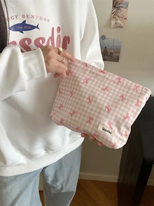 Pink checkered cotton makeup bag with bow pattern held by a model in a bright room