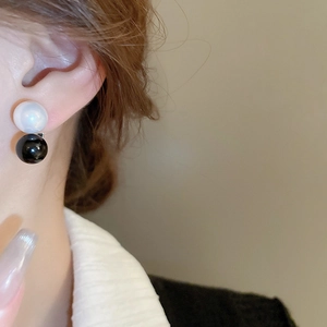 Close-up of minimalist black and white pearl geometric earrings worn by a model