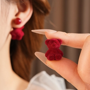 Detailed close-up of red flocked teddy bear earrings on ear showing plush texture
